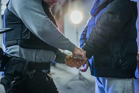 A police officer is putting handcuffs on a person with a black puffer jacket.