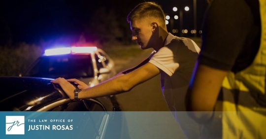 person with hands on side of car being looked at by an officer, police car with lights on in the back
